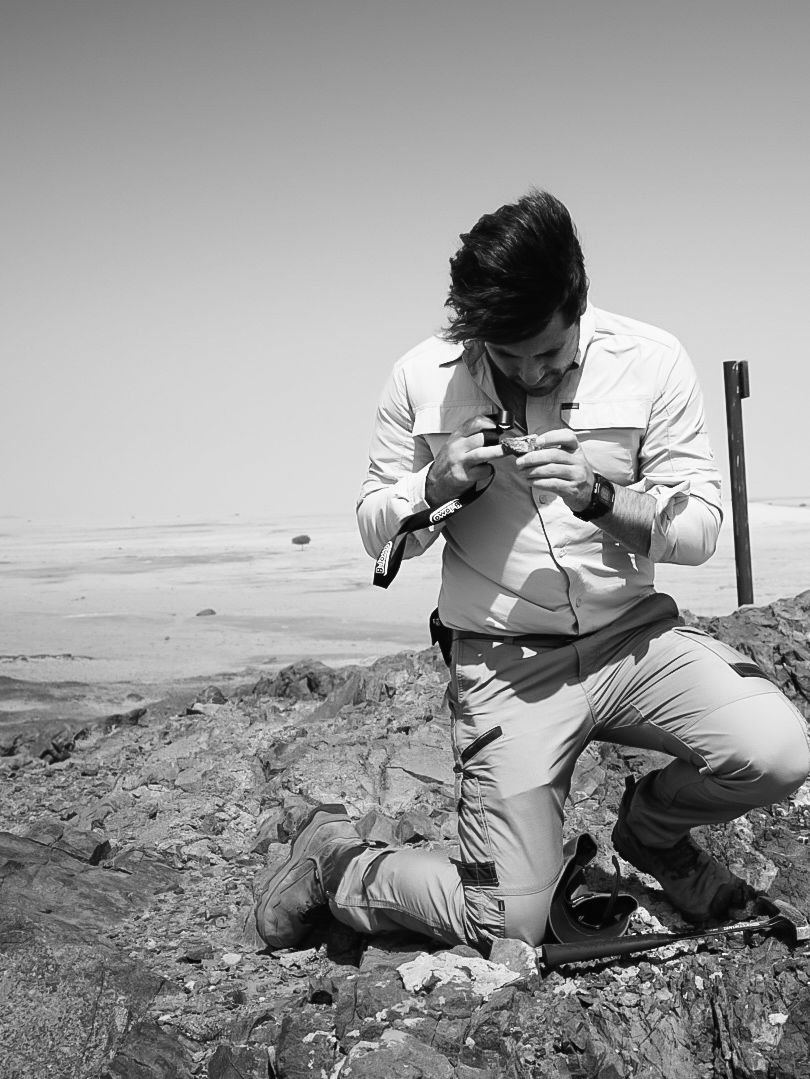 Geologist examining a rock sample with a hand lens in a desert outcrop