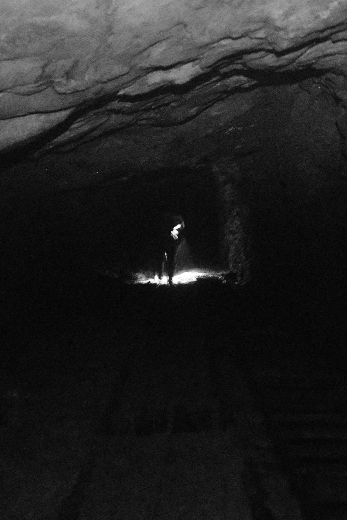Lone figure lit by a headlamp at the end of a mine tunnel